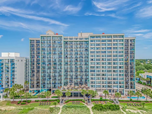 A high-rise hotel with multiple balconies, a swimming pool, and a landscaped garden area.