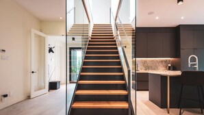 Un interior moderno con una escalera de madera, una zona de cocina y una puerta de cristal que da a otra habitación.