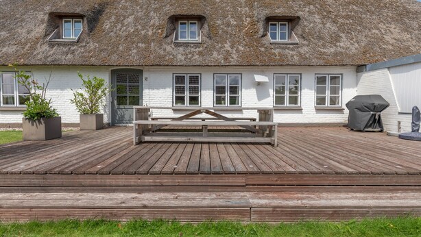 Una casa tradizionale con tetto di paglia, un pontile in legno, un’area salotto coperta e piante in vaso.
