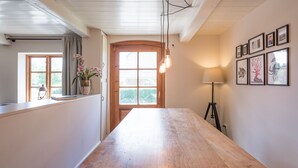 Una stanza spaziosa con un tavolo in legno, una finestra con tende, una lampada e quadri appesi al muro.
