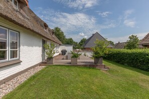 Une maison à l’extérieur blanc et au toit de chaume, avec une terrasse dallée et une pelouse bien entretenue.