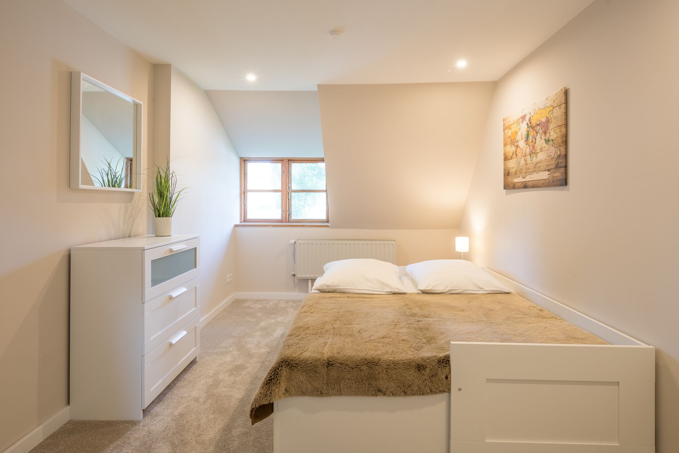 A bedroom with a bed, a dresser, a radiator, a window, and a painting on the wall.