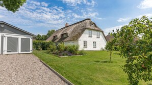 Una casa con tetto di paglia, esterno bianco e vialetto in ghiaia.