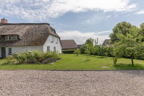 Une maison avec un toit de chaume, une pelouse bien entretenue et une allée gravillonnée.