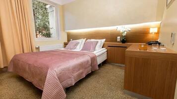 A hotel room with a bed, bedside table, lamp, and a view of greenery outside.