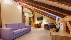 Una habitación moderna estilo loft con vigas de madera a la vista, un sofá morado, una mesa de madera con un florero y un televisor de pantalla plana montado en la pared.