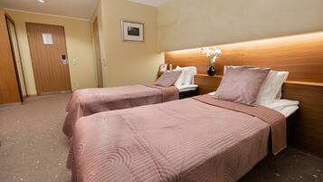 A hotel room with two beds, a wooden headboard, a framed picture on the wall, and a door.
