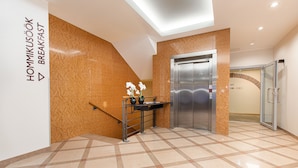 Un moderno vestíbulo de hotel con mostrador de recepción, un ascensor y una puerta de vidrio que da a una zona de duchas.