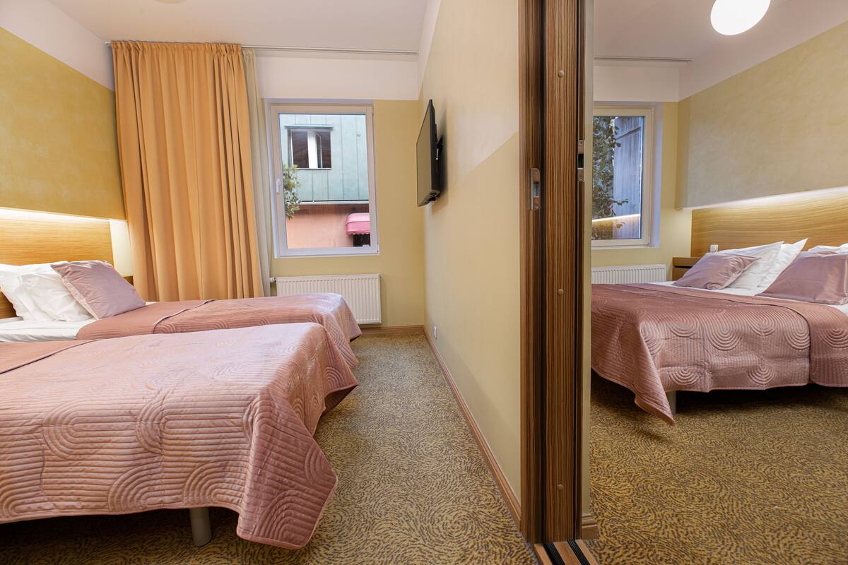 A hotel room with two beds, a window, a television, and a view of the outside balcony.