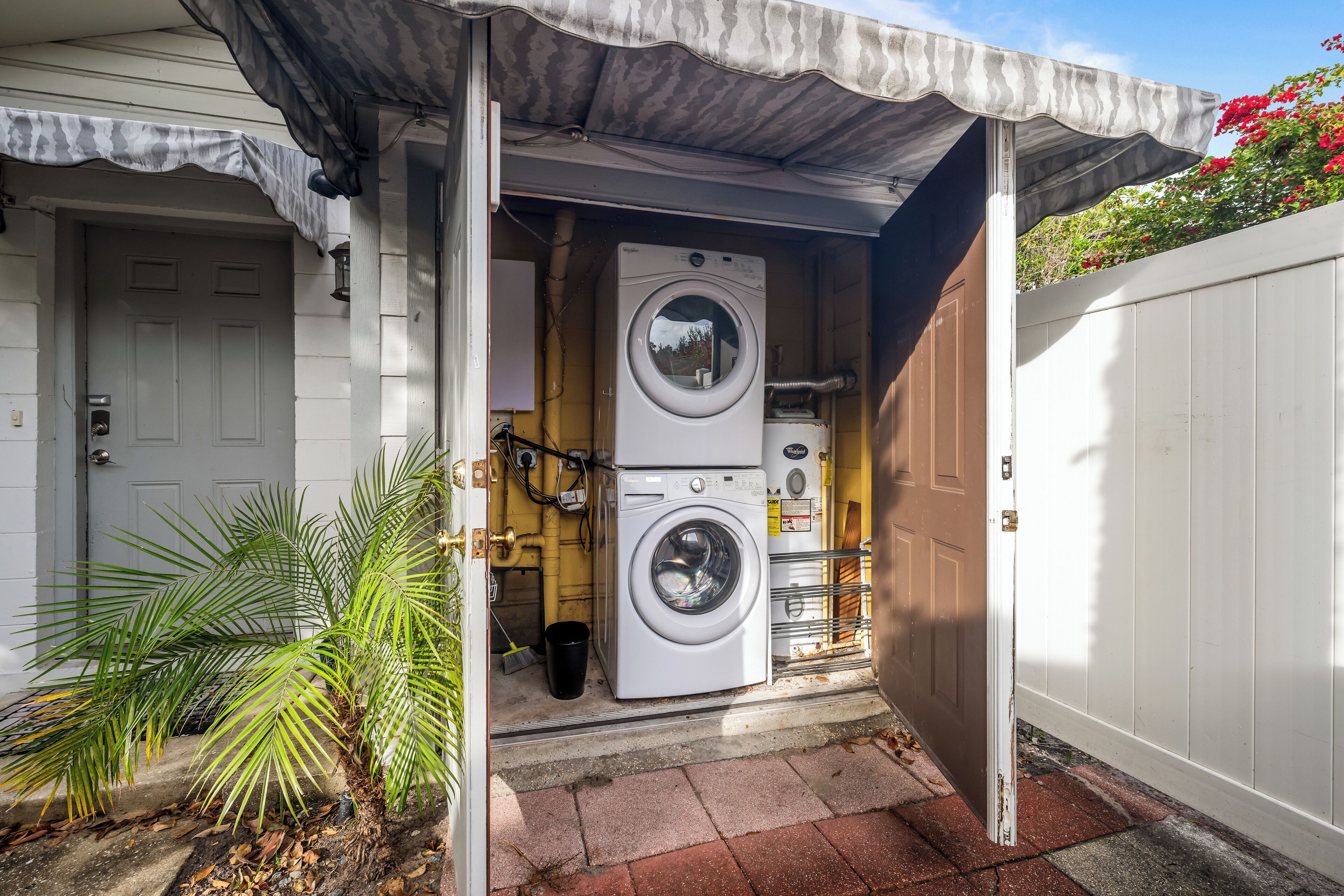 A laundry room with two stacked washers and dryers, a small palm tree, and a white door.