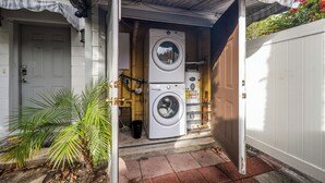 Une buanderie équipée de deux machines à laver et de deux sèche-linge superposés, d’un petit palmier et d’une porte blanche.