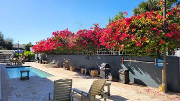 A poolside area with a barbecue grill, lounge chairs, and a wall covered in vibrant pink flowers.