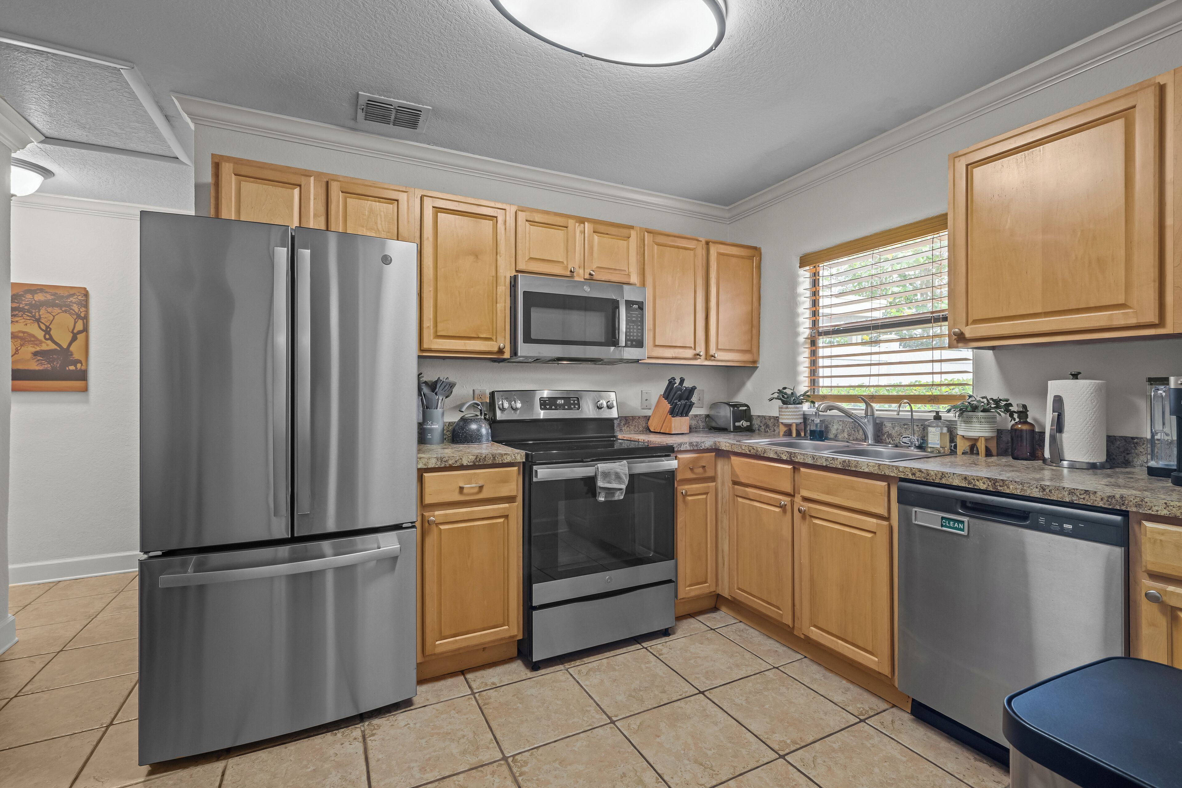 A modern kitchen with stainless steel appliances, wooden cabinets, and a tiled floor.