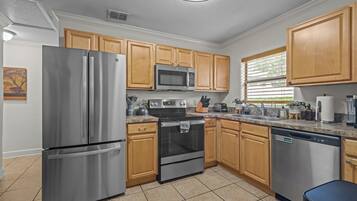 A modern kitchen with stainless steel appliances, wooden cabinets, and a tiled floor.