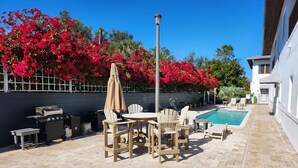 Une terrasse extérieure avec une piscine, entourée de fleurs rouges et d’un bâtiment blanc.
