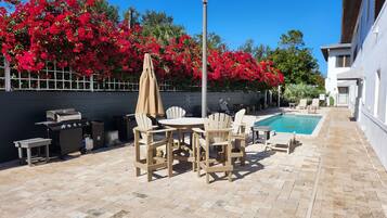 An outdoor patio with a pool, surrounded by red flowers and a white building.
