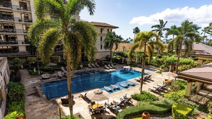 Un hotel con piscina, sillas de descanso y palmeras.