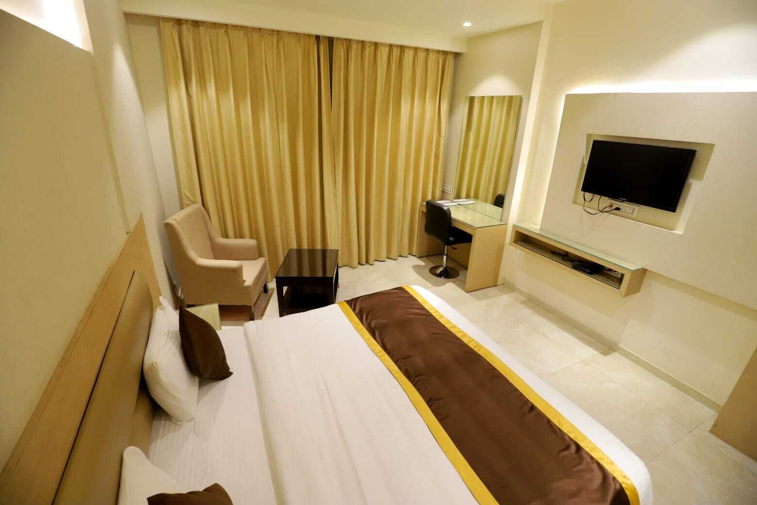 A hotel room with a bed, a desk, a chair, a TV, and curtains.