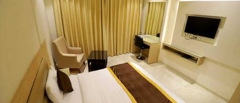 A hotel room with a bed, a desk, a chair, a TV, and curtains.