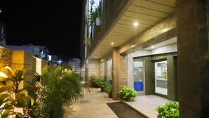 A well-lit outdoor corridor with potted plants, a doormat, and a door leading to a room with a view. - Hotel Skylark (Bareilly)