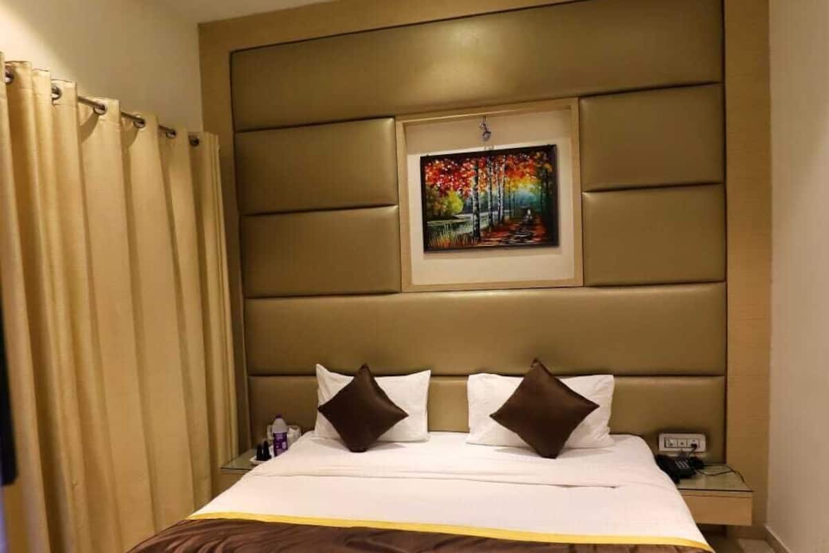 A hotel room with a large bed, a ceiling fan, a painting on the wall, and a nightstand with a phone.