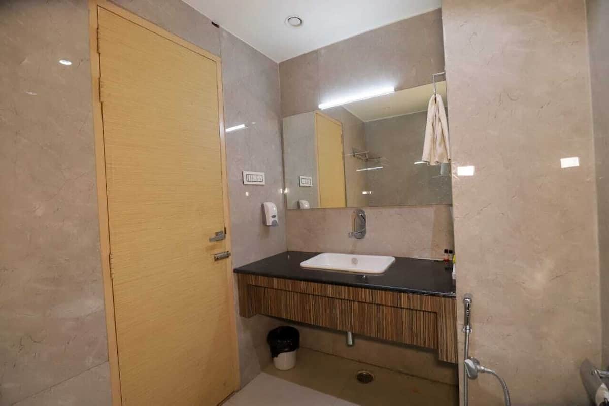 A modern bathroom with a wooden door, a black countertop sink, a mirror, and a shower area.