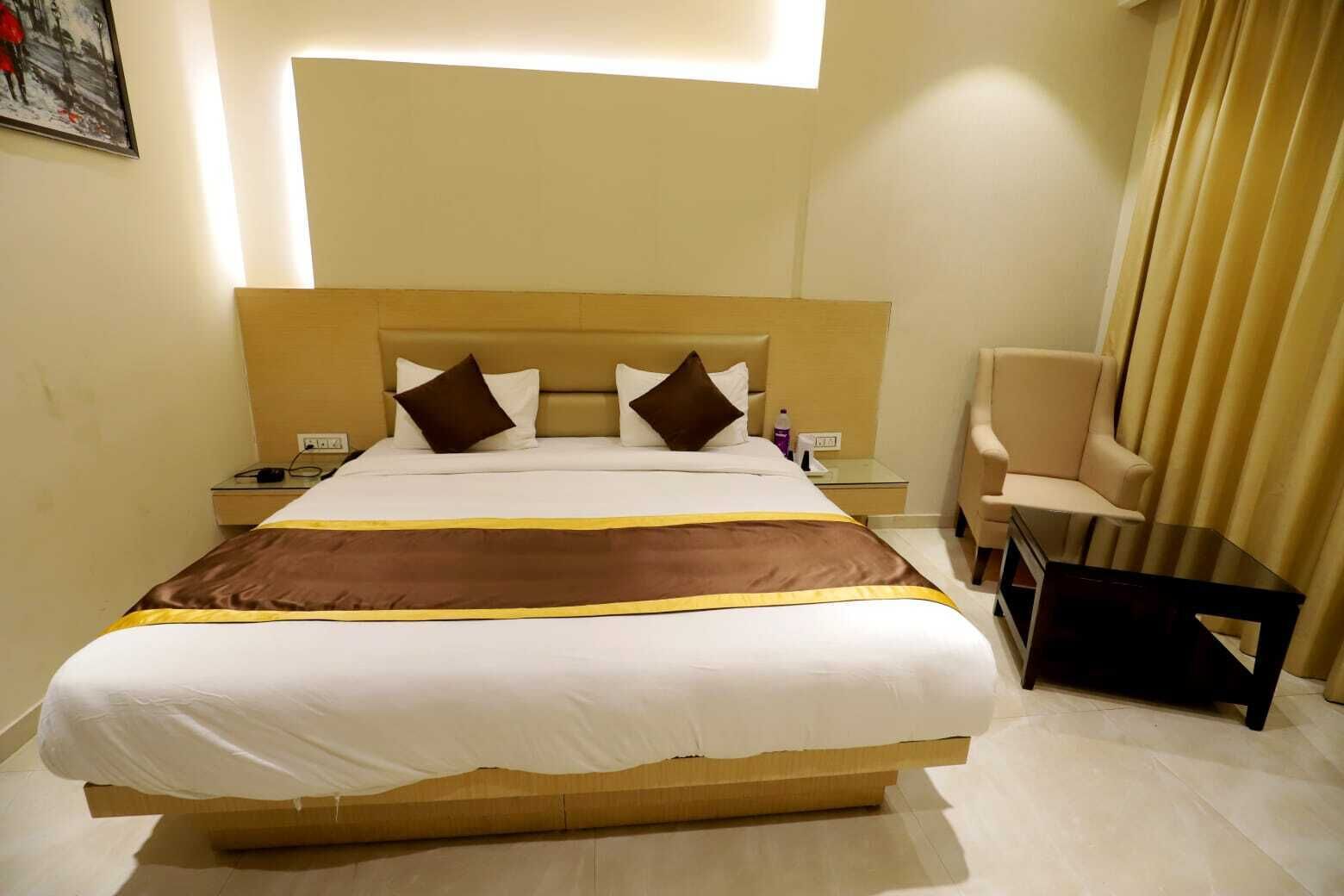 A hotel room with a large bed, a bedside table with a lamp, a chair, and a small table.
