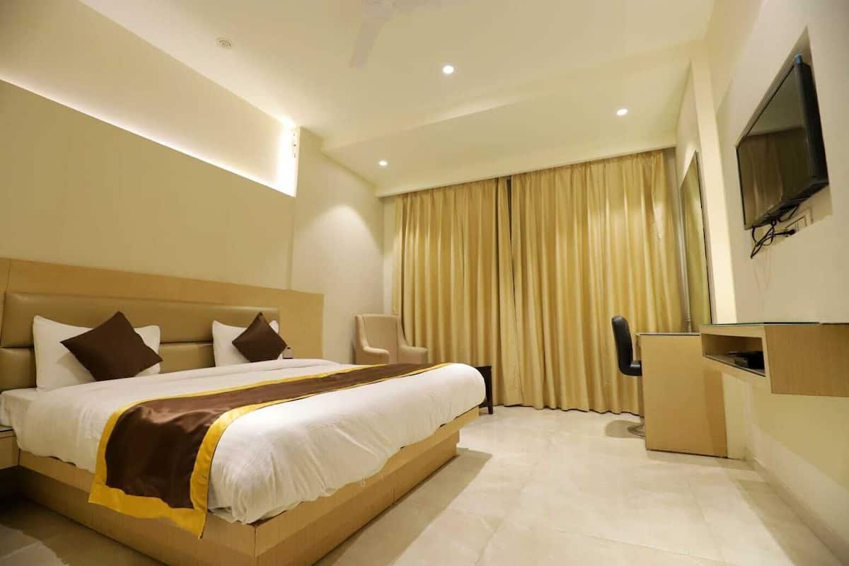 A hotel room with a large bed, a desk, a chair, a TV, and a curtain.