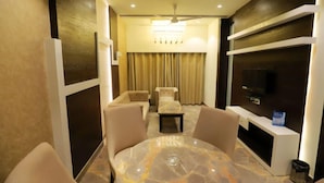 A modern living room with a marble table, beige sofas, a TV, and a ceiling fan. - Hotel Skylark (Bareilly)