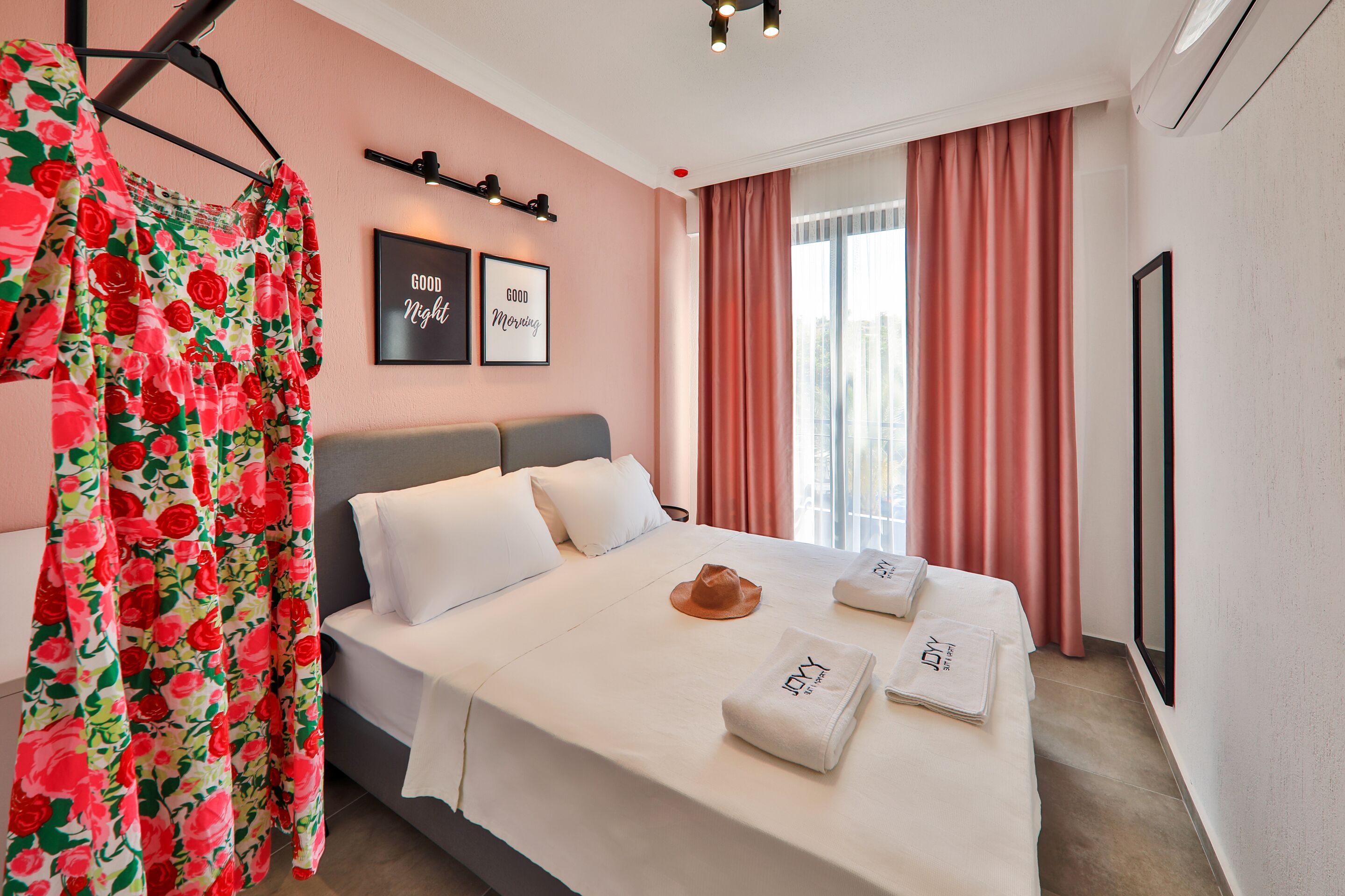 Habitación de hotel con cama, ropa de cama blanca, un sombrero, toallas, una cita enmarcada en la pared y una ventana con cortinas.