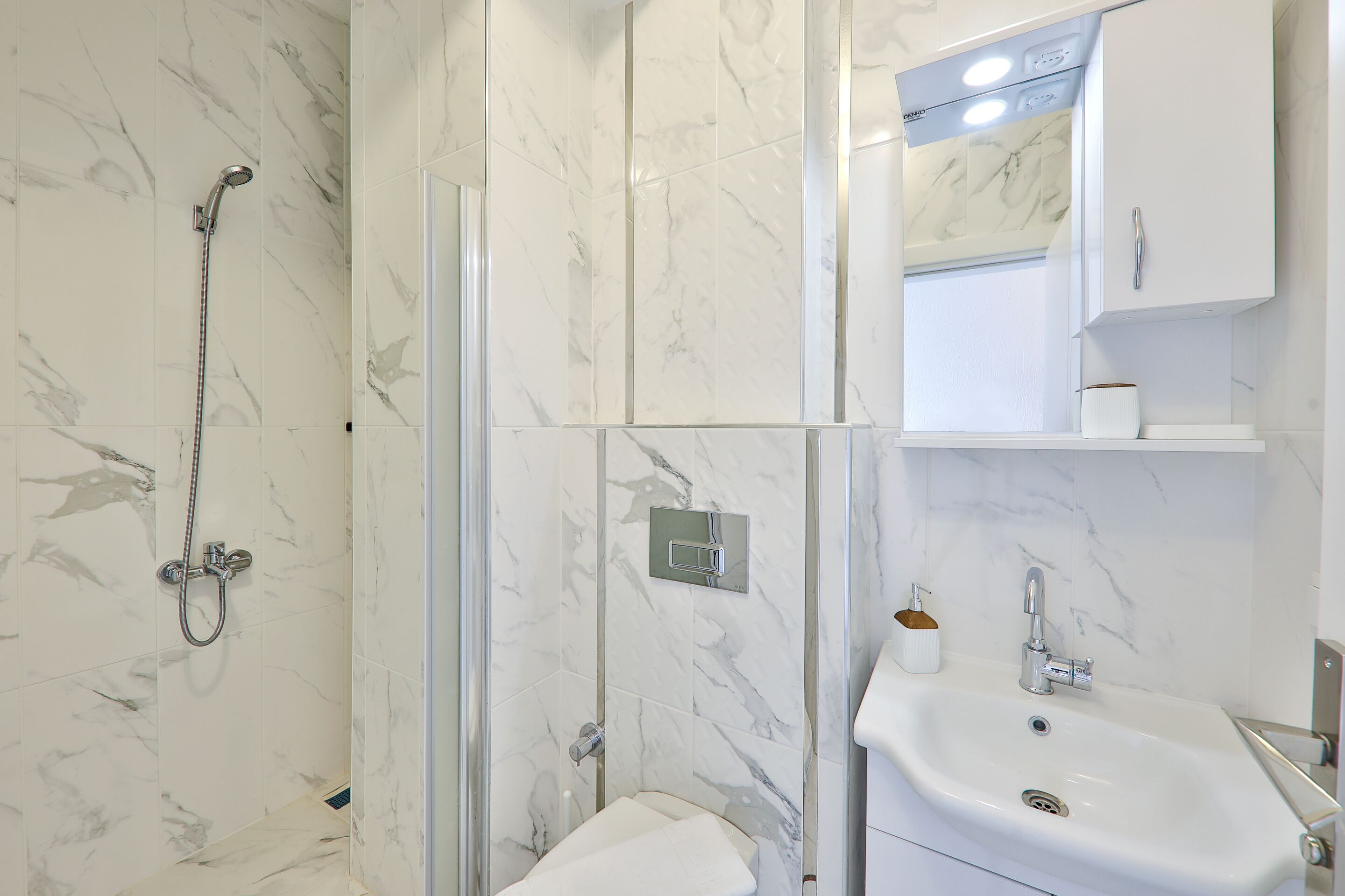 A modern bathroom with a glass-enclosed shower, a white sink, and a marble-tiled wall.
