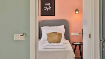 Une chambre d’hôtel avec un lit, un panier, un panneau encadré portant l’inscription « BONNE NUIT » et une lampe fixée au mur.