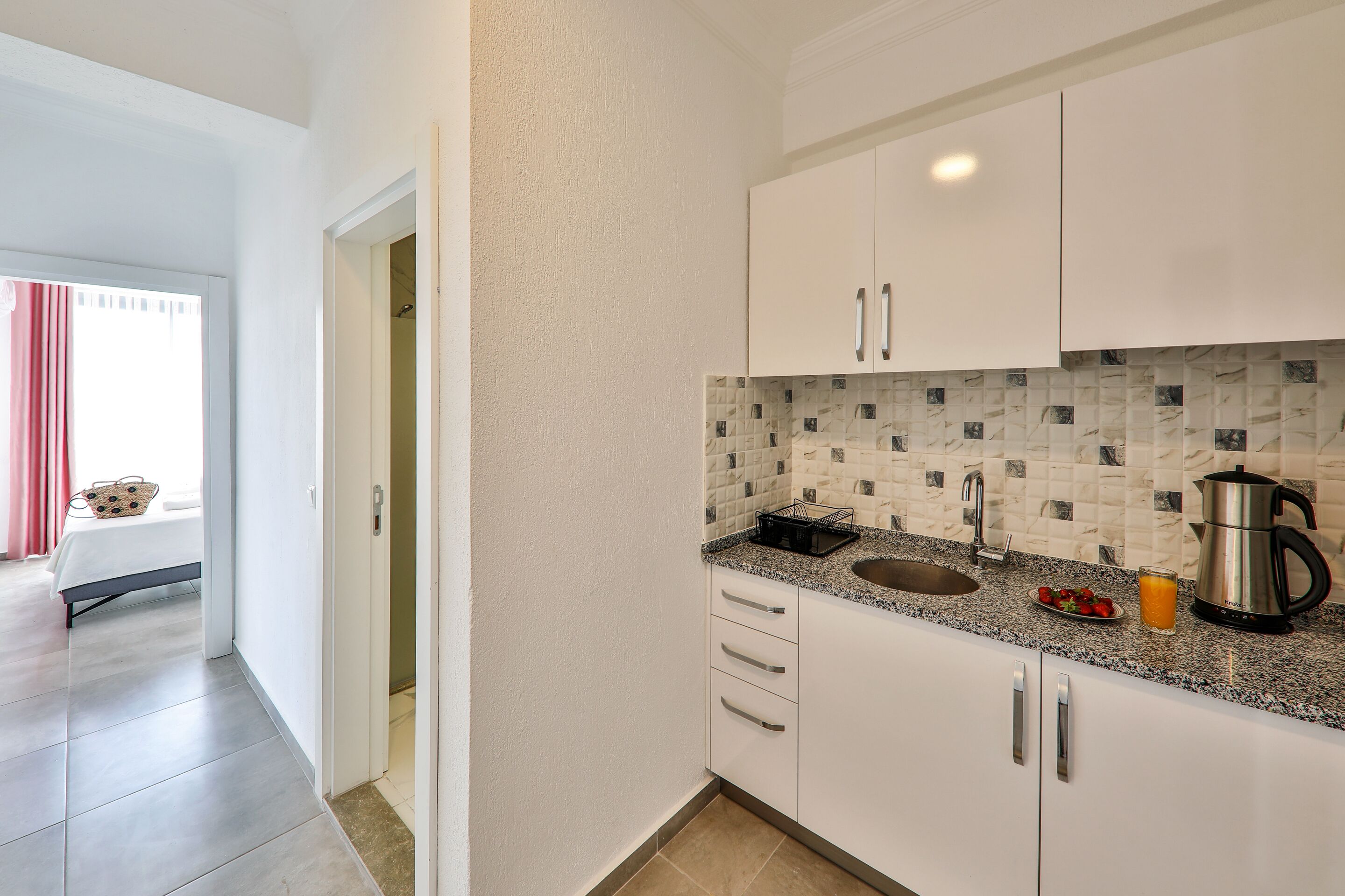 Et moderne køkken med hvide skabe, en granitbordplade, en vask, kaffemaskine og et flisebeklædt backsplash.