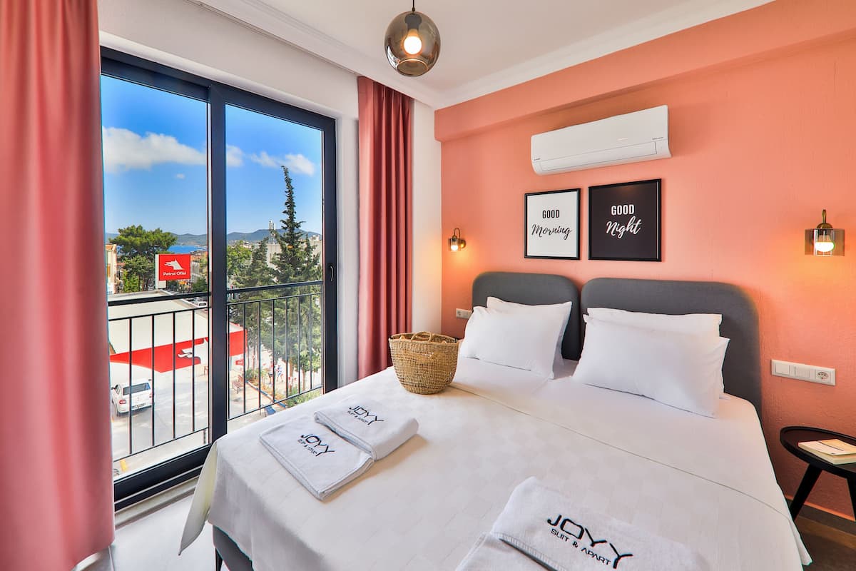 Quarto de hotel com cama, janela com vista para a cidade, varanda e ar condicionado fixado na parede.