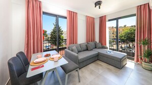 Una sala de estar moderna con un sofá seccional gris, una mesa de comedor con platos rosas y ventanas amplias con cortinas rojas.
