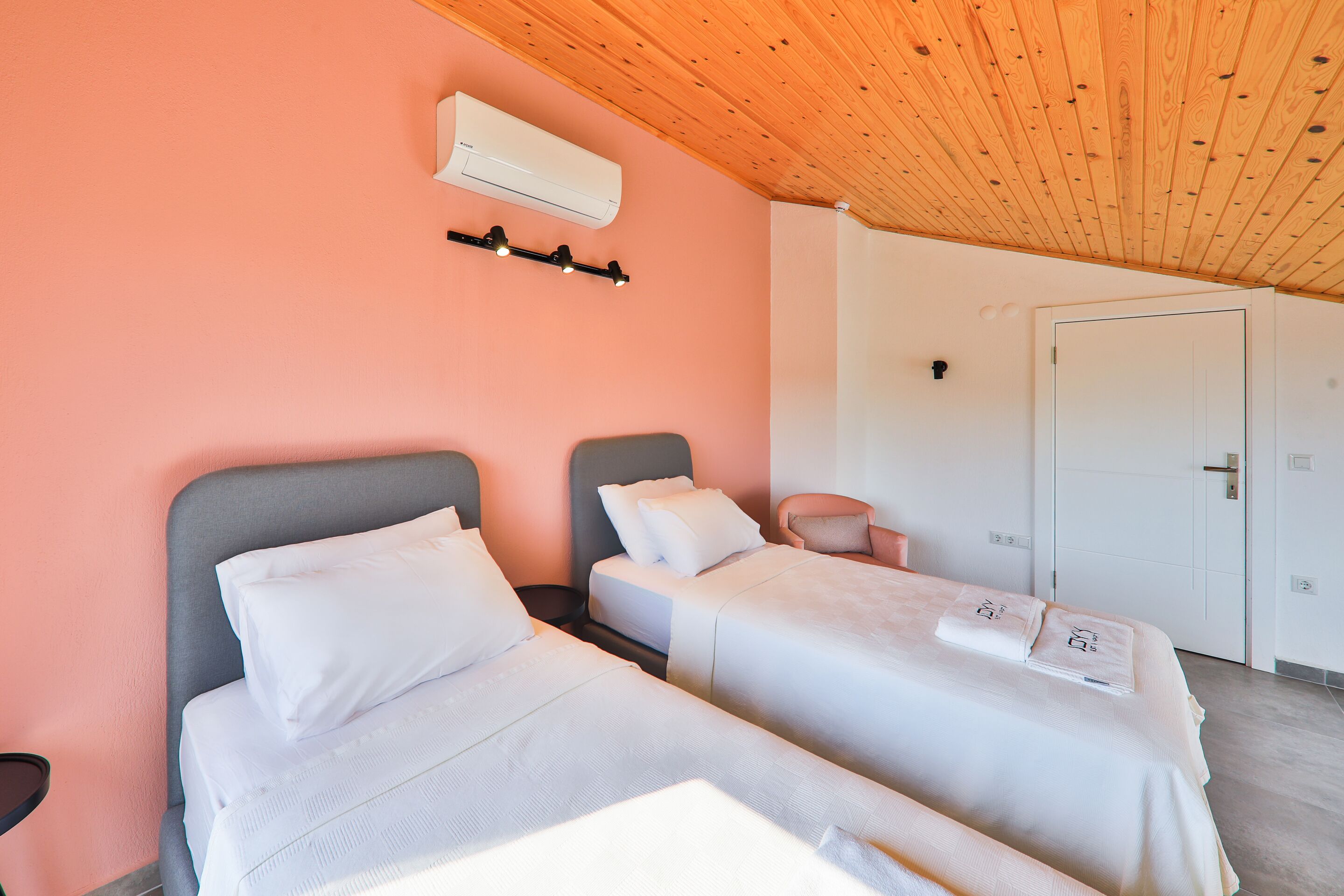 A hotel room with two beds, a wooden ceiling, an air conditioning unit, and a white door.