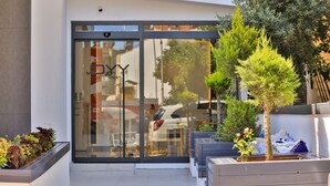 Una entrada moderna a un edificio con puerta de vidrio, asientos al aire libre y plantas en macetas.