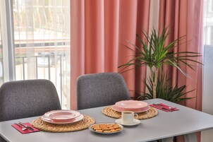 A dining table set with plates, a cup, and cutlery, with a plant and curtains in the background.