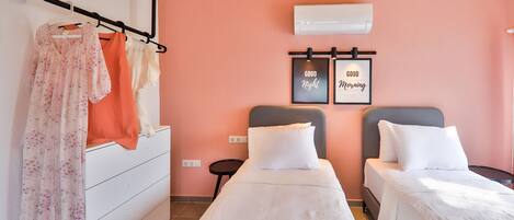 A bedroom with two beds, a white dresser, a hanging rack with clothes, and two framed signs saying "Good Night" and "Good Morning".