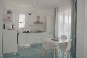 Une cuisine moderne avec des meubles blancs, une table à manger avec des chaises et une fenêtre avec des rideaux.