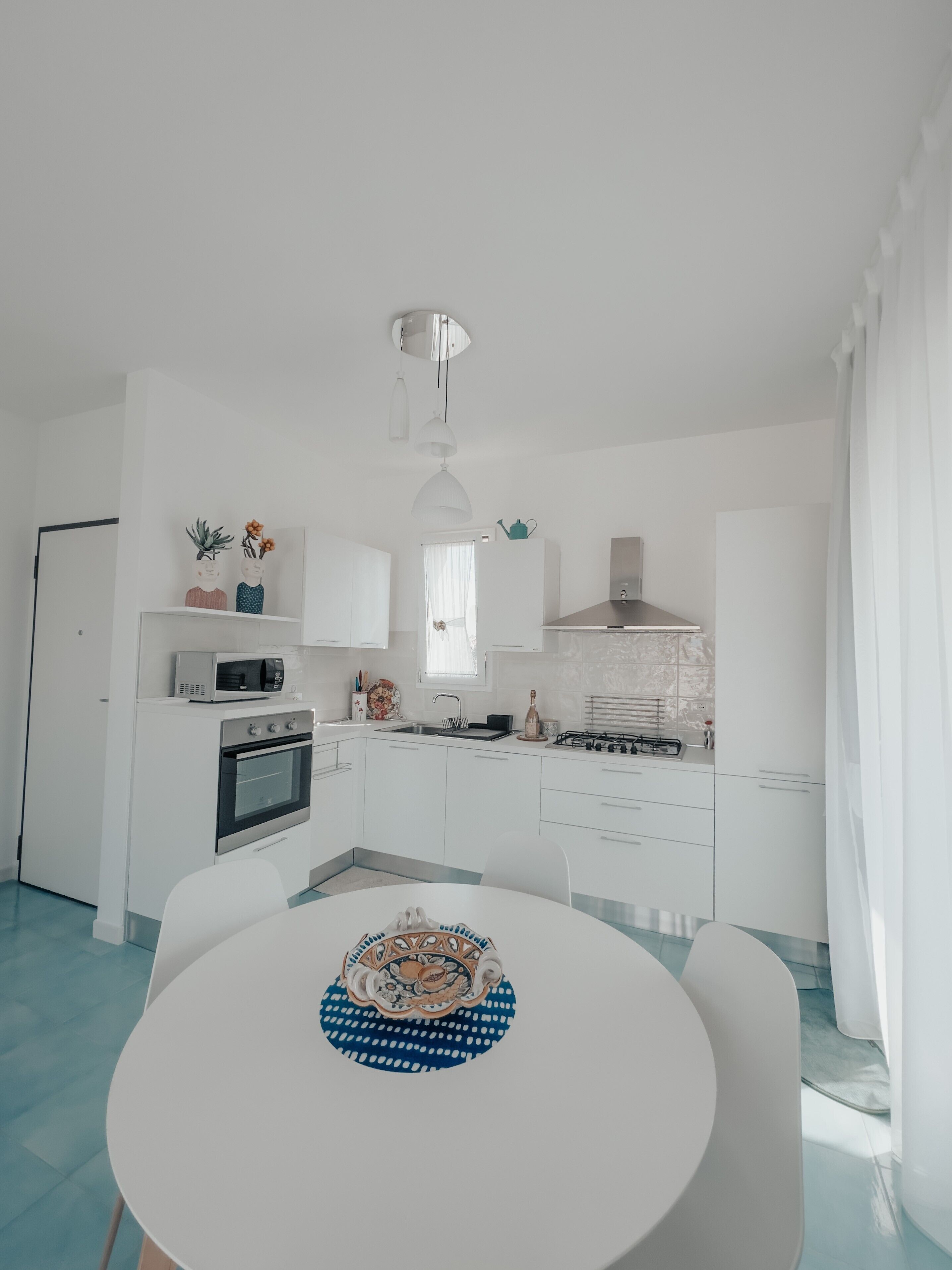 A modern kitchen with white cabinets, a dining table with a blue and white patterned centerpiece, and a white ceiling.