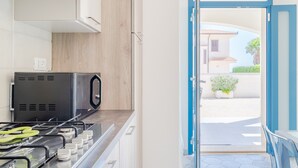 A kitchen with a gas stove, microwave, and a view of a street through an open door. - Holiday Home "MisMar 2" with Sea View, Garden & Wi-Fi (Noto)