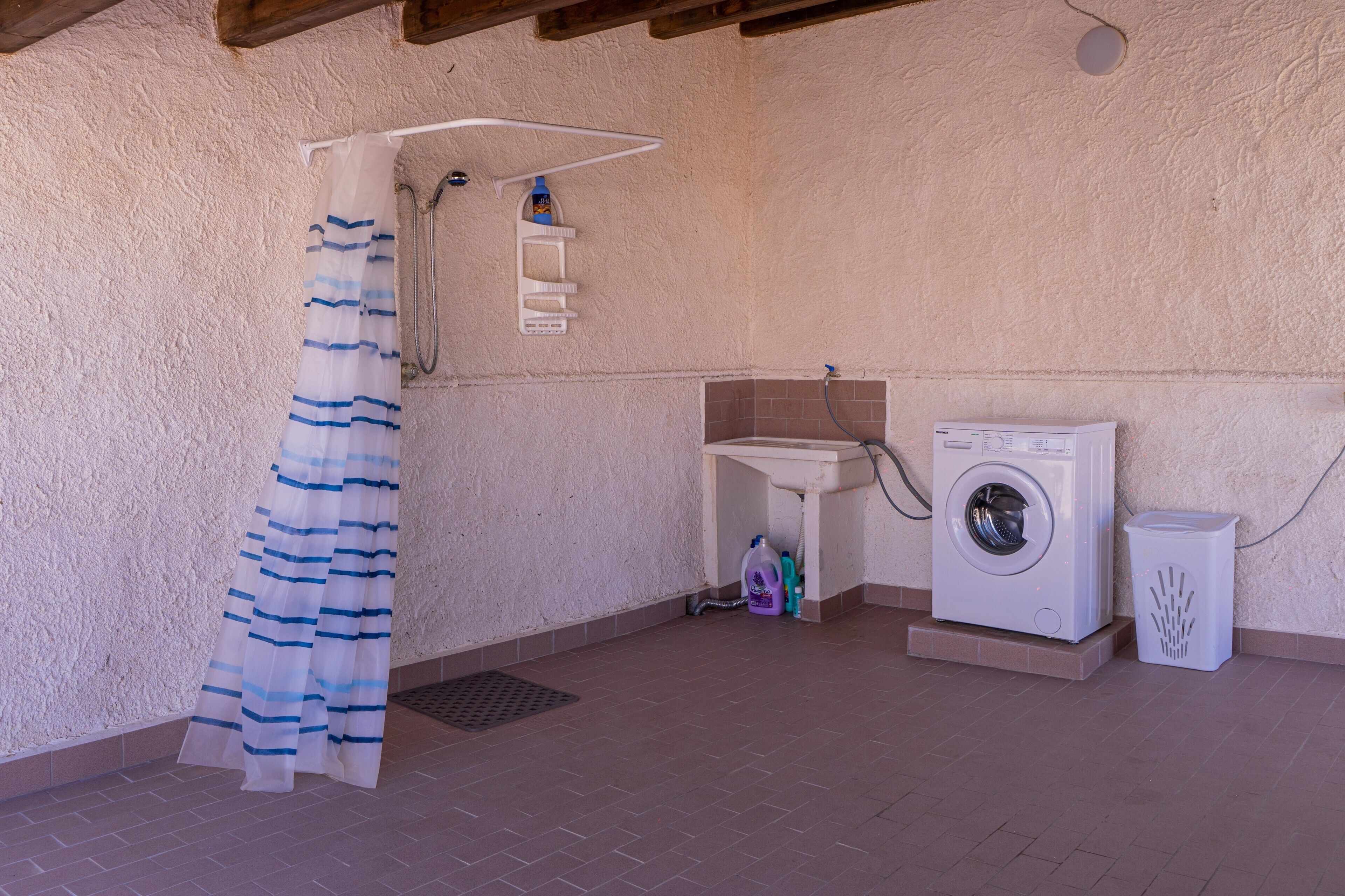 Ein Badezimmer mit Dusche, Waschbecken, Waschmaschine und Mülleimer.