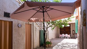 Un patio con una sombrilla, una puerta de madera, una mesa con sillas y plantas en macetas.