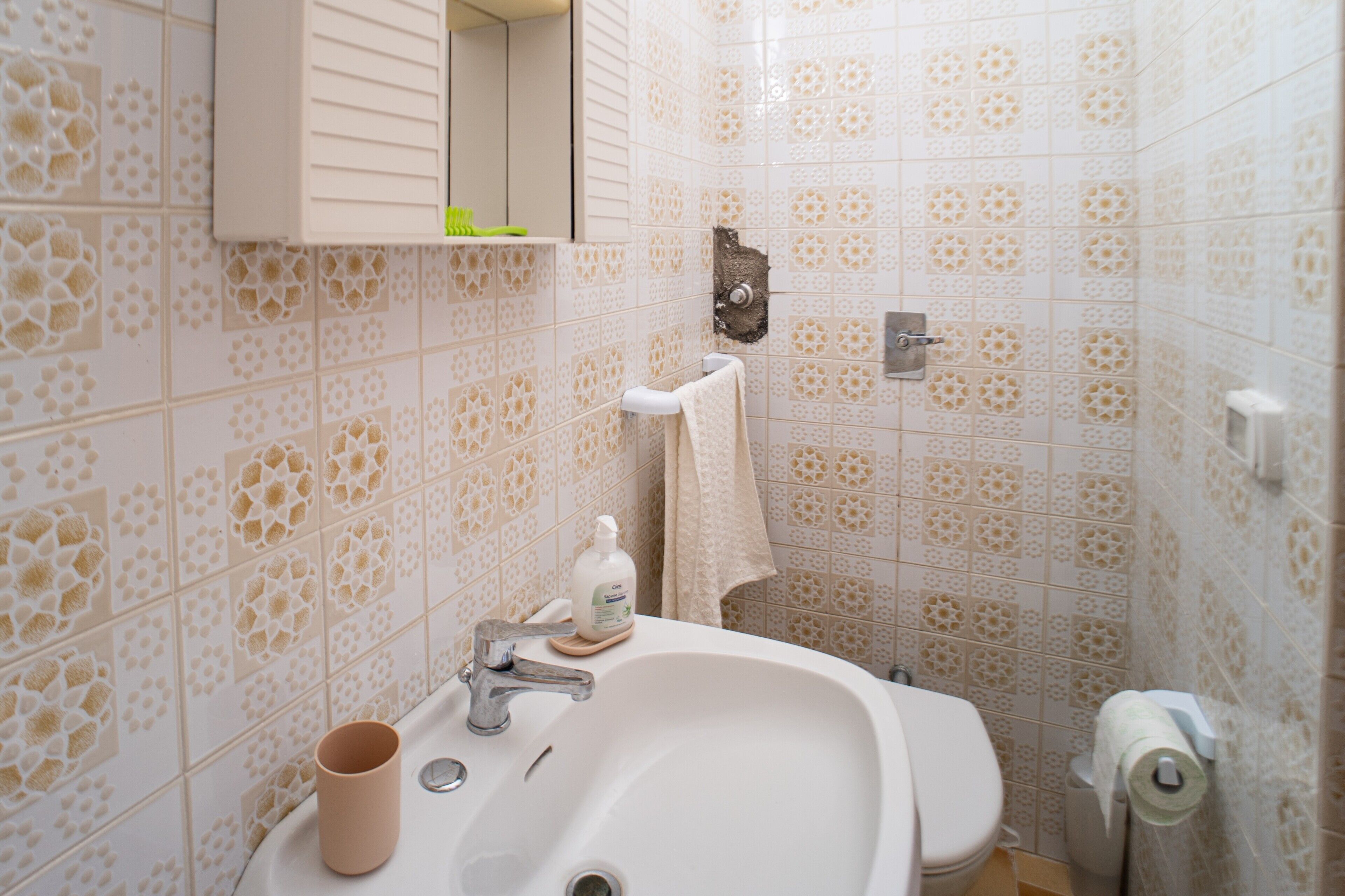 Un baño con baldosas estampadas, un lavabo, un espejo, una toalla y un inodoro.