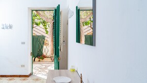Una habitación con suelo de baldosas, una mesa de madera con un plato blanco, una puerta verde y un espejo en la pared.