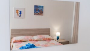 Un dormitorio con cabecera de madera, cama con colcha de estampado coral, mesita de noche con lámpara y dos cuadros en la pared.