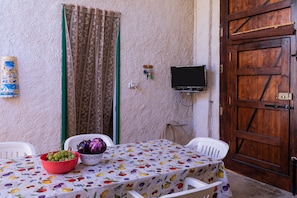 A room with a table covered by a fruit-patterned tablecloth, a wooden door, and a television mounted on the wall.