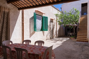 An outdoor patio with a table and chairs, a covered seating area, and a narrow alleyway.