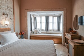 Um quarto com uma cama grande, um assento junto à janela, um penteado de madeira e uma TV fixada na parede.
